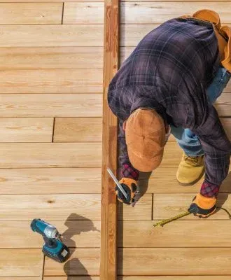 A man is measuring a piece of wood on a wooden deck.