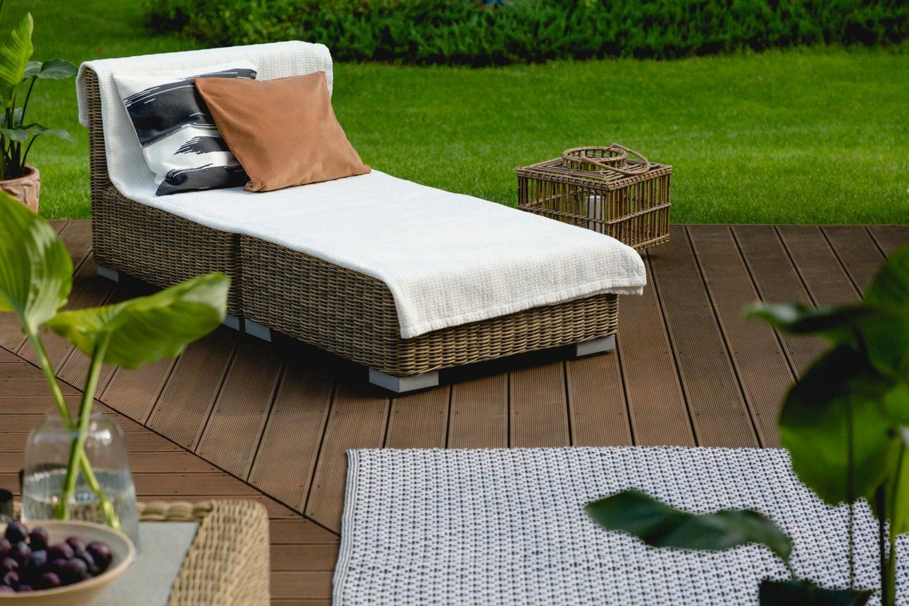 A wicker lounge chair is sitting on a wooden deck.