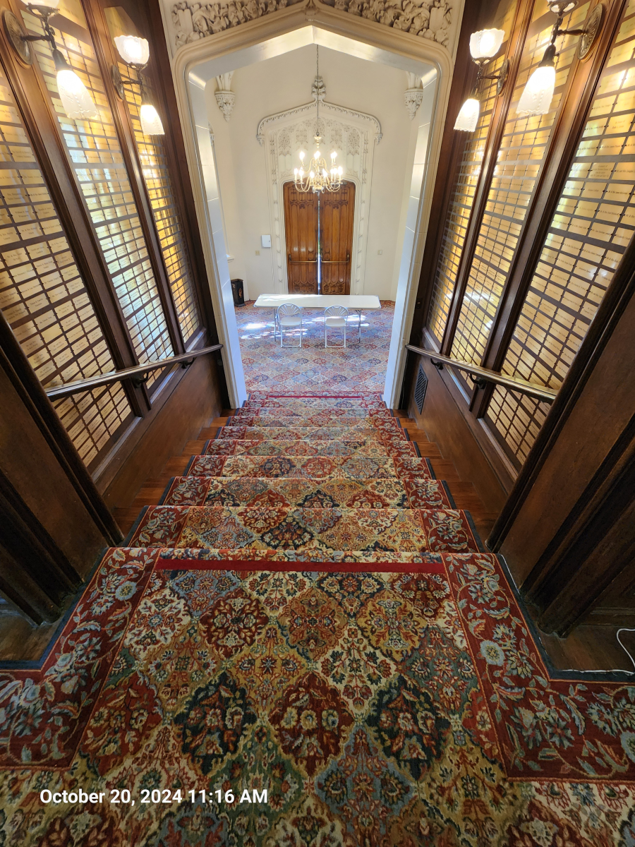 A carpeted staircase leads up to a wide doorway with a chandelier and double doors in a wood-paneled hallway.