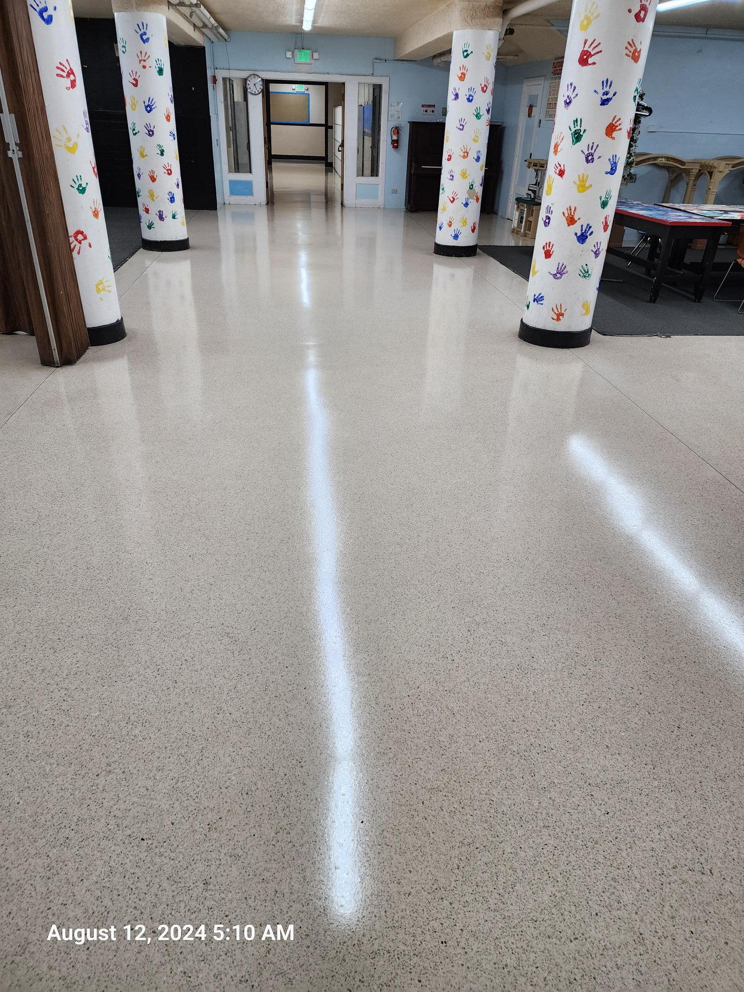 A wide, polished hallway with speckled floors and columns decorated with colorful painted handprints.