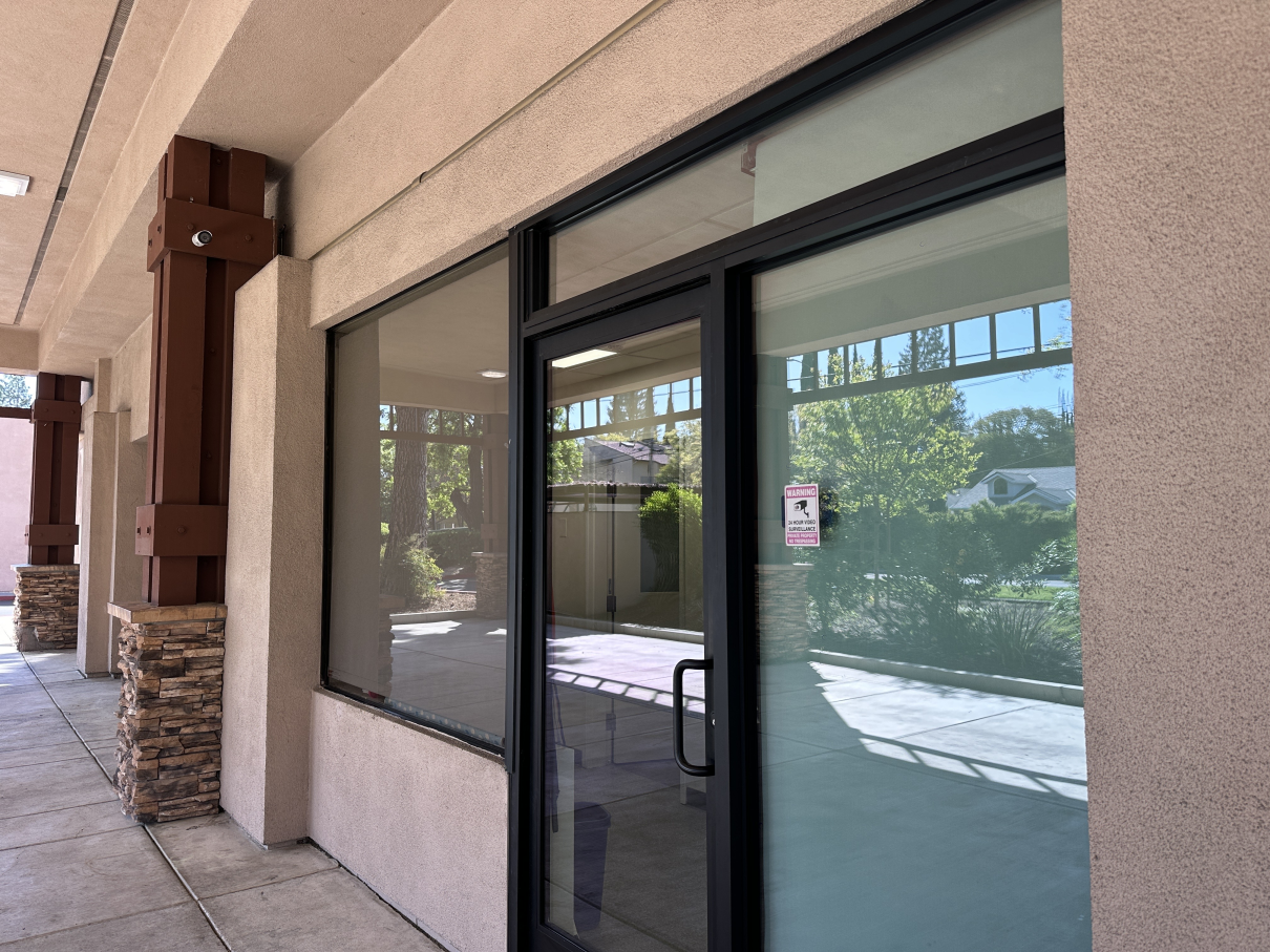 An exterior view of a vacant commercial storefront featuring glass doors and windows, under a covered walkway.