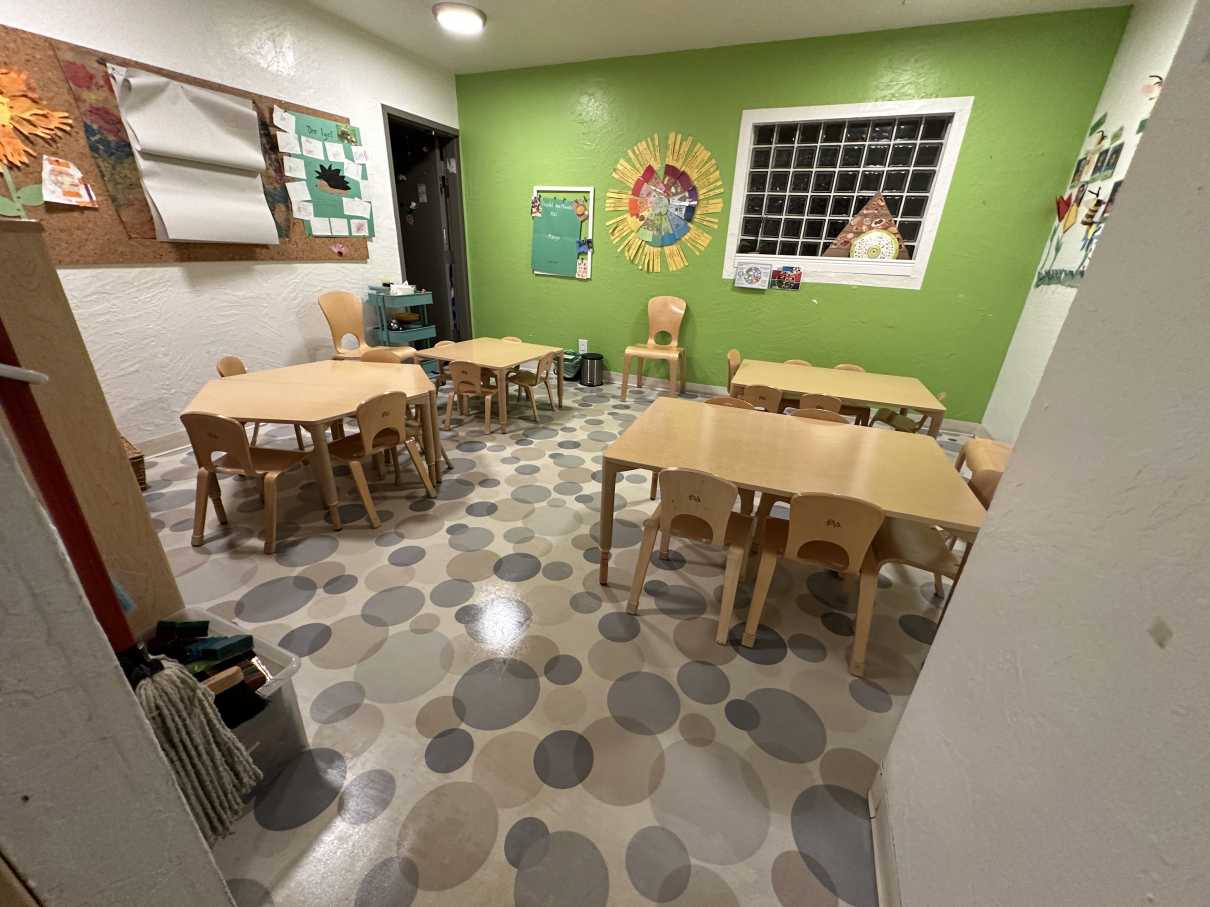 A colorful classroom with child-sized wooden tables and chairs set on a floor featuring various shades of gray circles.