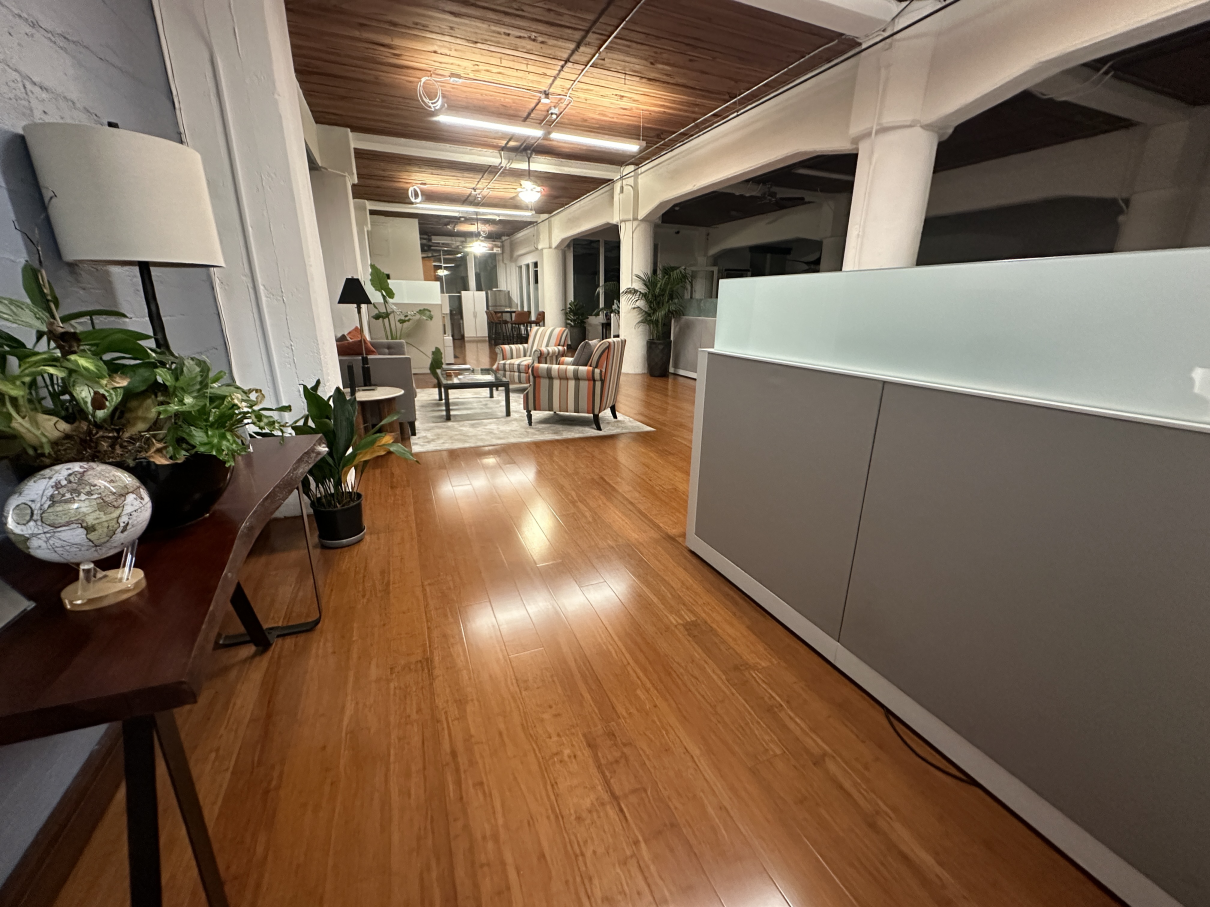 A modern office lobby with hardwood floors, a desk, a houseplant, a globe, and a seating area in the background.