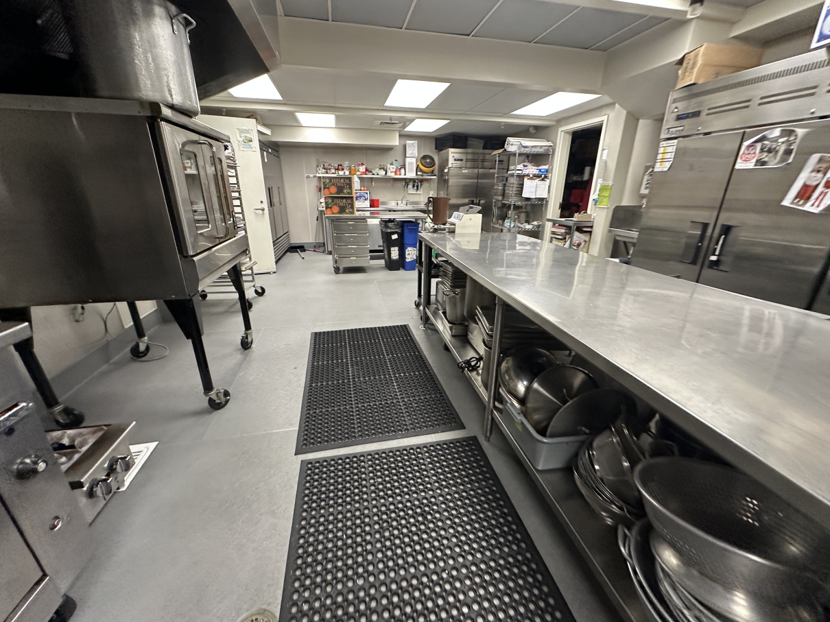 A commercial kitchen featuring stainless steel prep tables, industrial appliances, and black rubber floor mats.