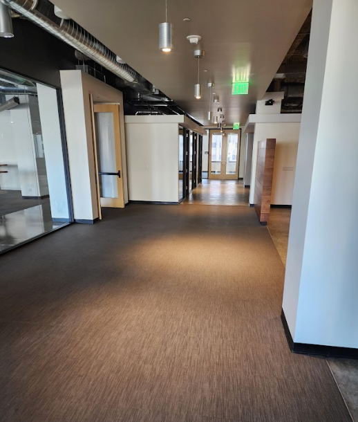 A long, empty school hallway with terrazzo floors featuring a central star design, blue floor mats, and dark trim walls.