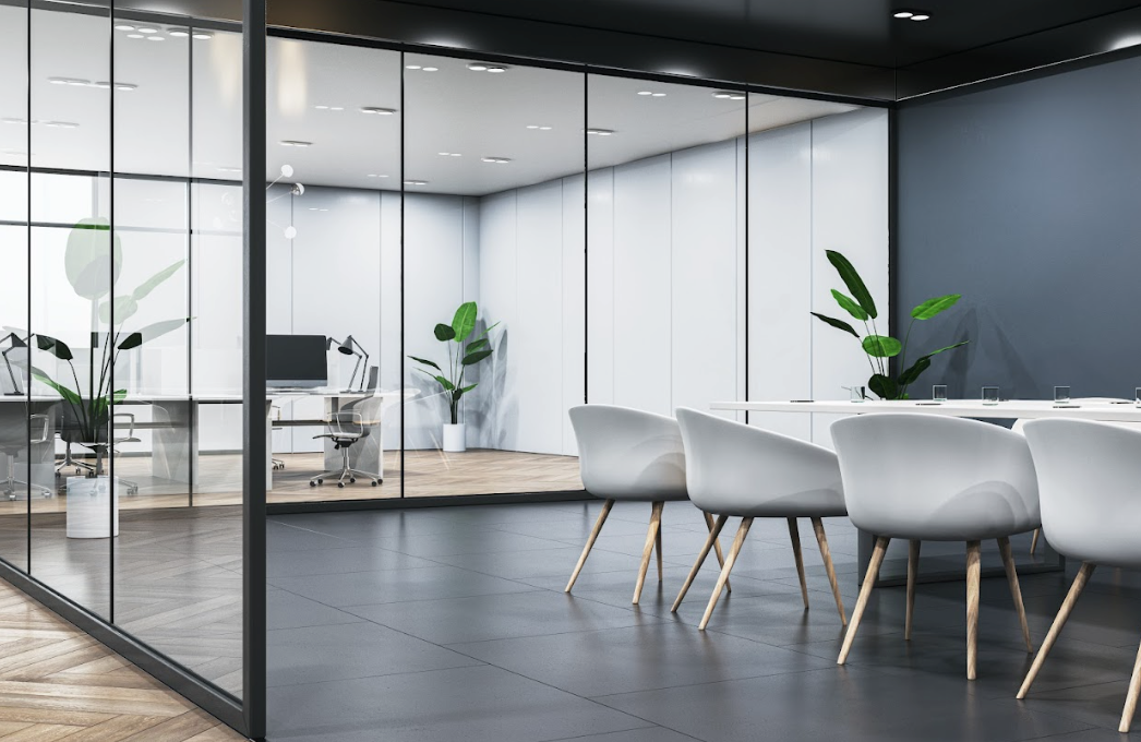 Modern office space with desks and chairs arranged along windows and a blue wall, featuring a geometric patterned carpet.