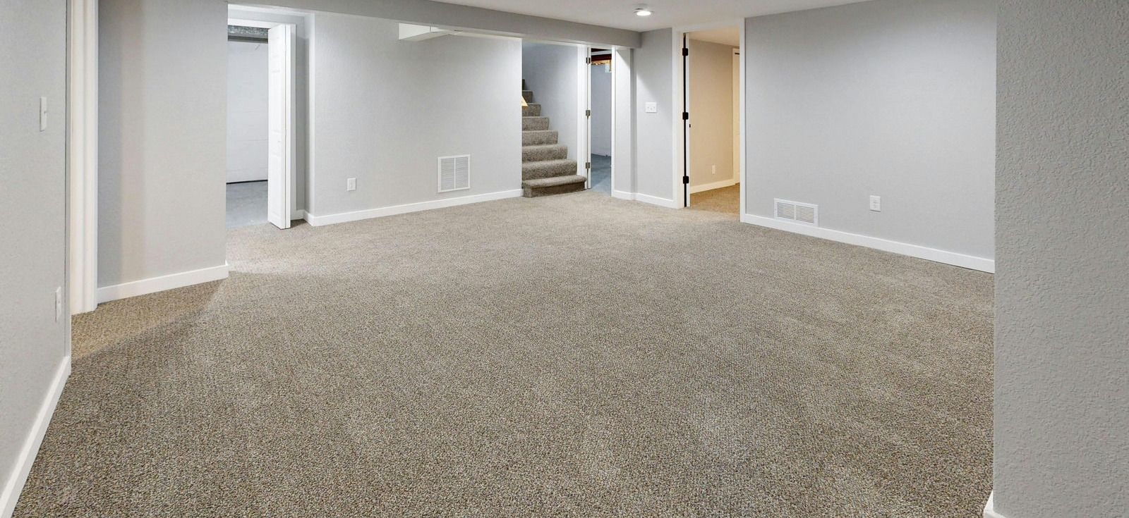 Empty carpeted basement room with gray walls, recessed lighting, and stairs in the back.