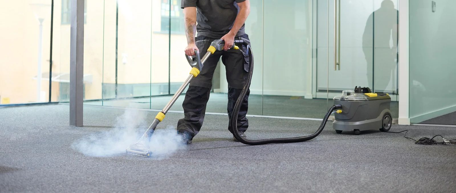 Worker pressure washing a carpeted floor indoors with a hose and machine
