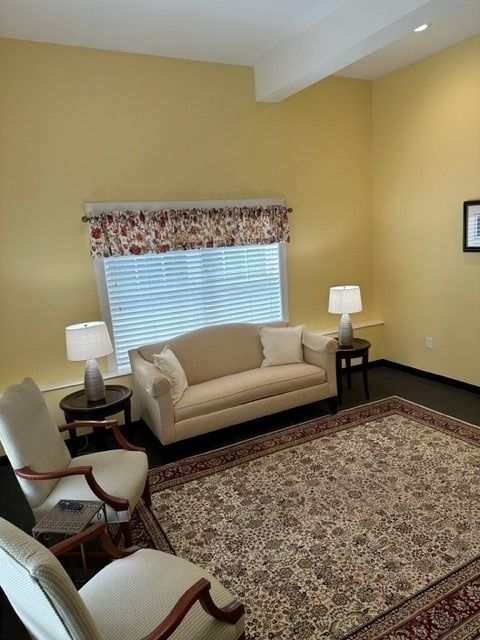 Beige living room with sofa, armchairs, lamps, patterned rug, and window blinds