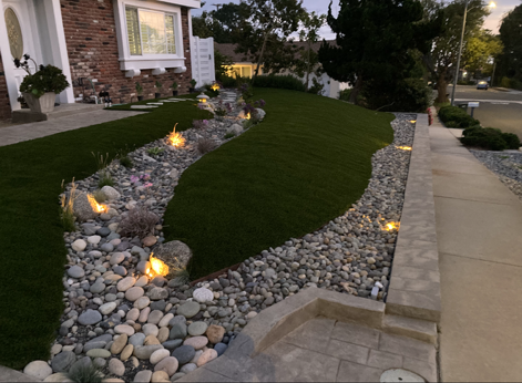 Front yard with stone landscaping, artificial turf, and low lighting at dusk.