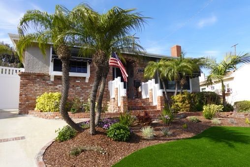 House with brick facade, palm trees, and American flag on a sunny day.