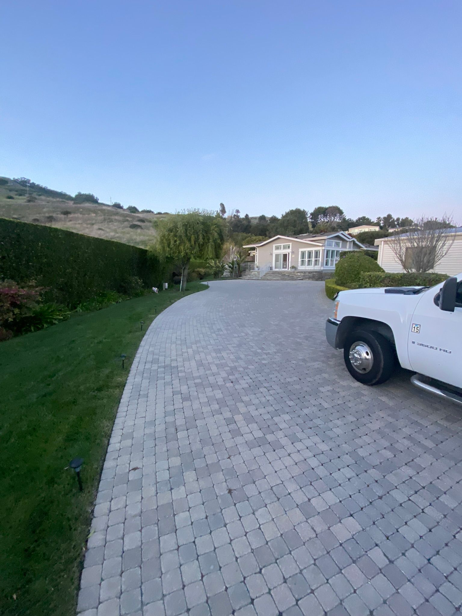 A white truck parked on a brick driveway in front of a house with a hillside background.