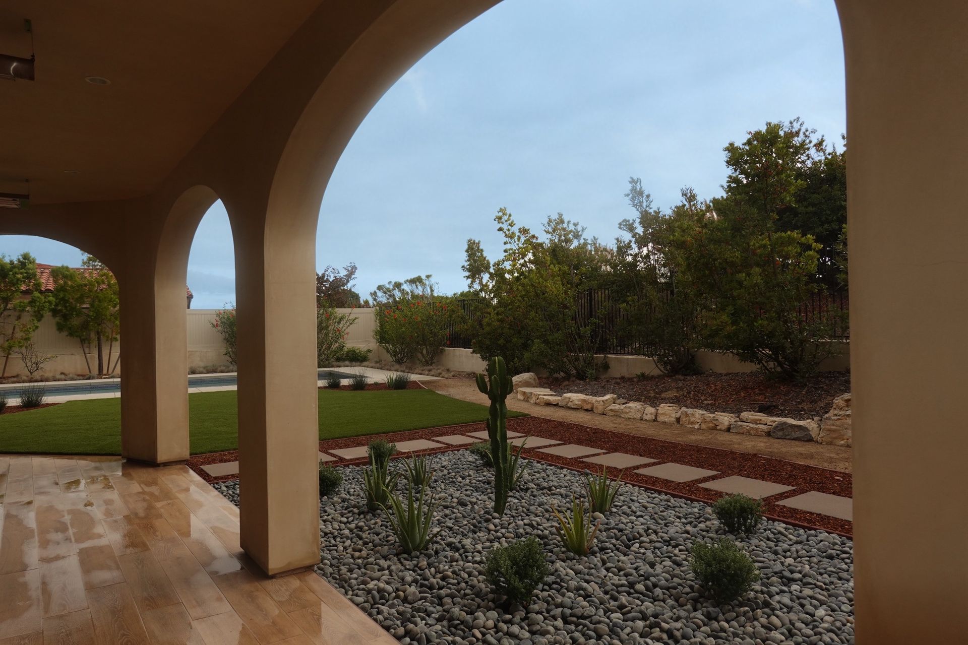 Covered patio overlooking a landscaped backyard with lawn, trees, and stone walkway