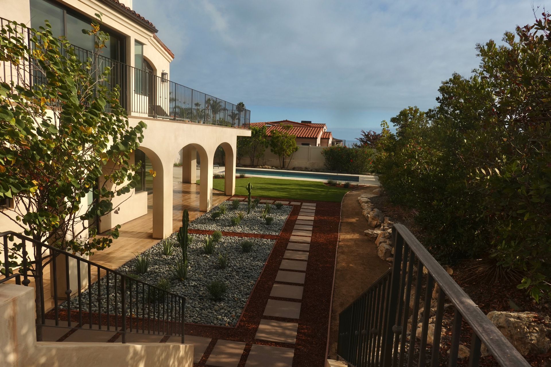 Mediterranean-style house with arched porch overlooking a landscaped garden and stone path at sunset