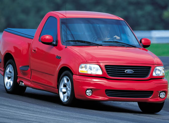 A red ford truck is driving down a road