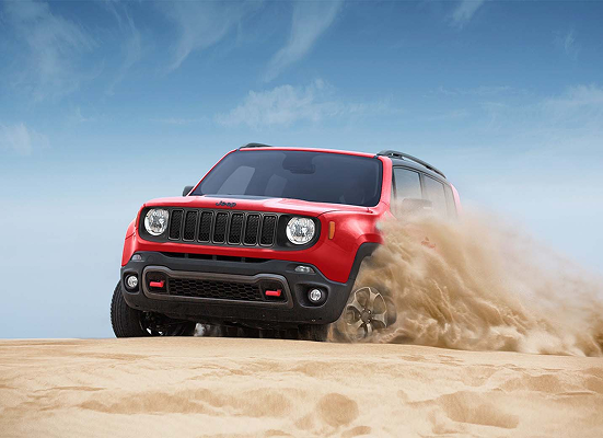 A red jeep renegade is driving through the sand in the desert.