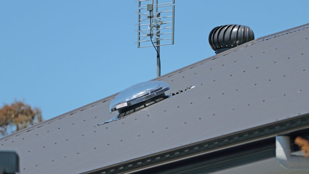 Solar-powered roof vent on a gray metal roof, with an antenna and a turbine vent visible — Ace Metal Roofing in Yamba, NSW