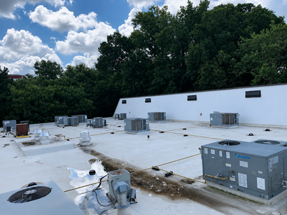 Flat rooftop with HVAC units, white surface, and trees under a cloudy sky.