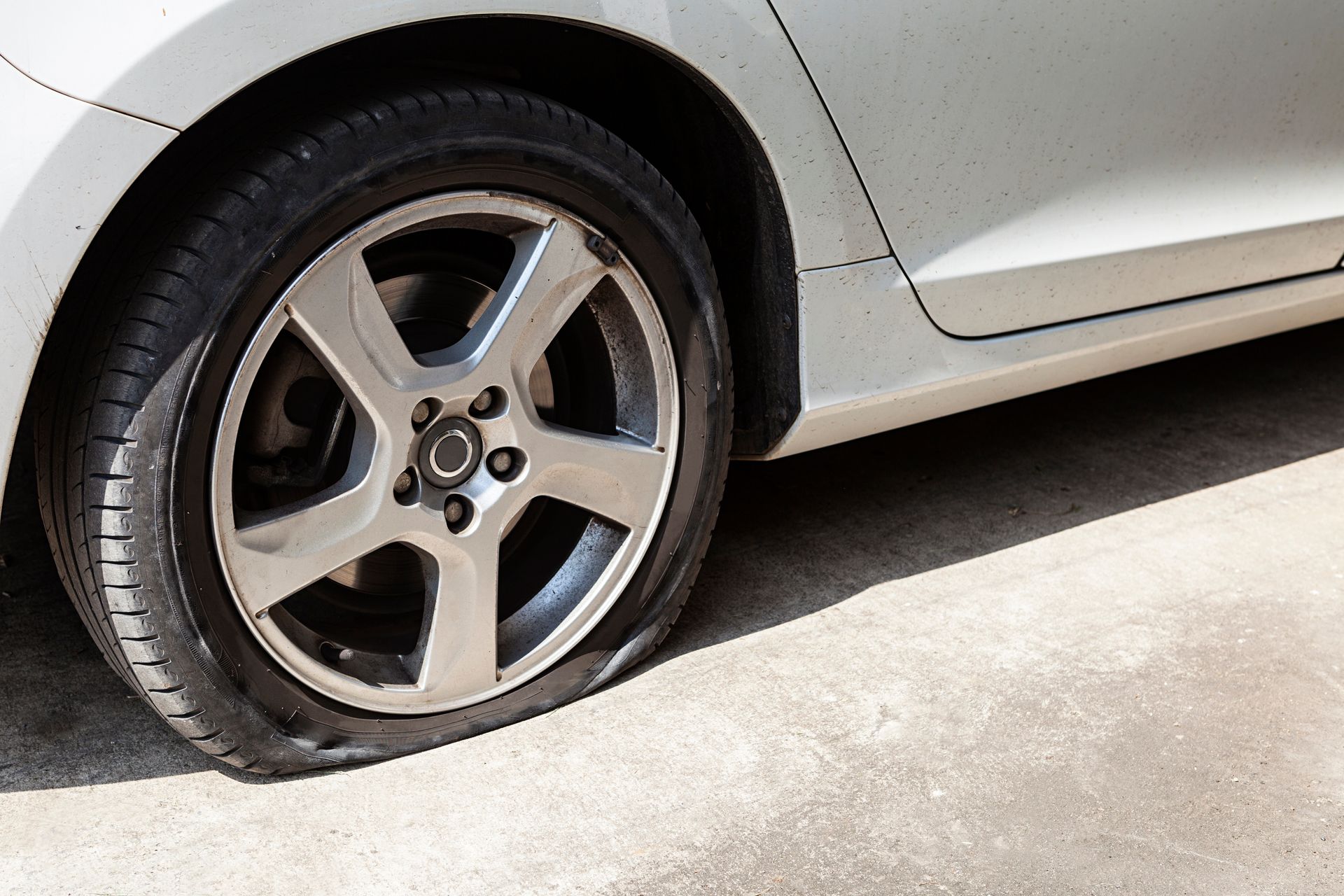 Car tire with flat tire on a silver car parked on a concrete surface