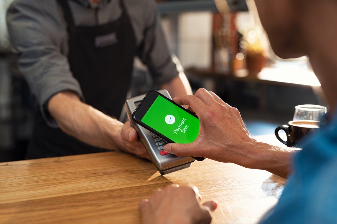 Person paying with phone at a cafe counter using contactless payment system.