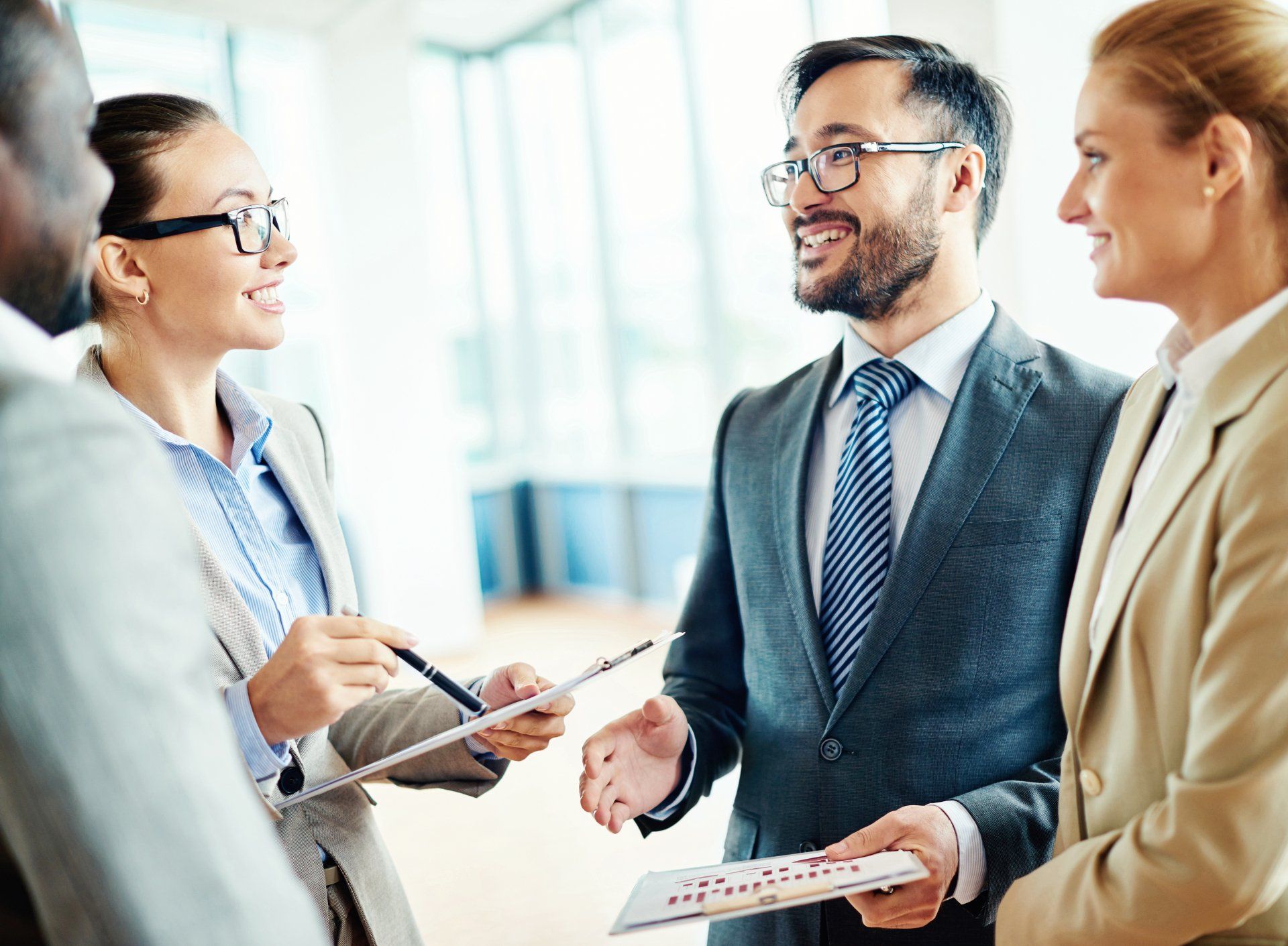 Businesspeople in suits discussing documents and smiling in a bright office.