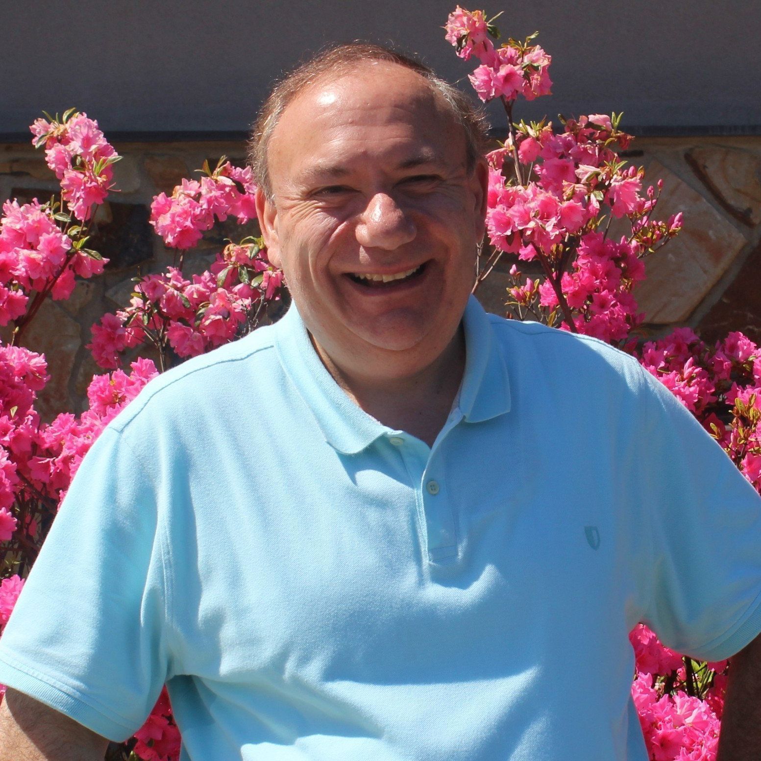 A man in a blue shirt is smiling in front of pink flowers