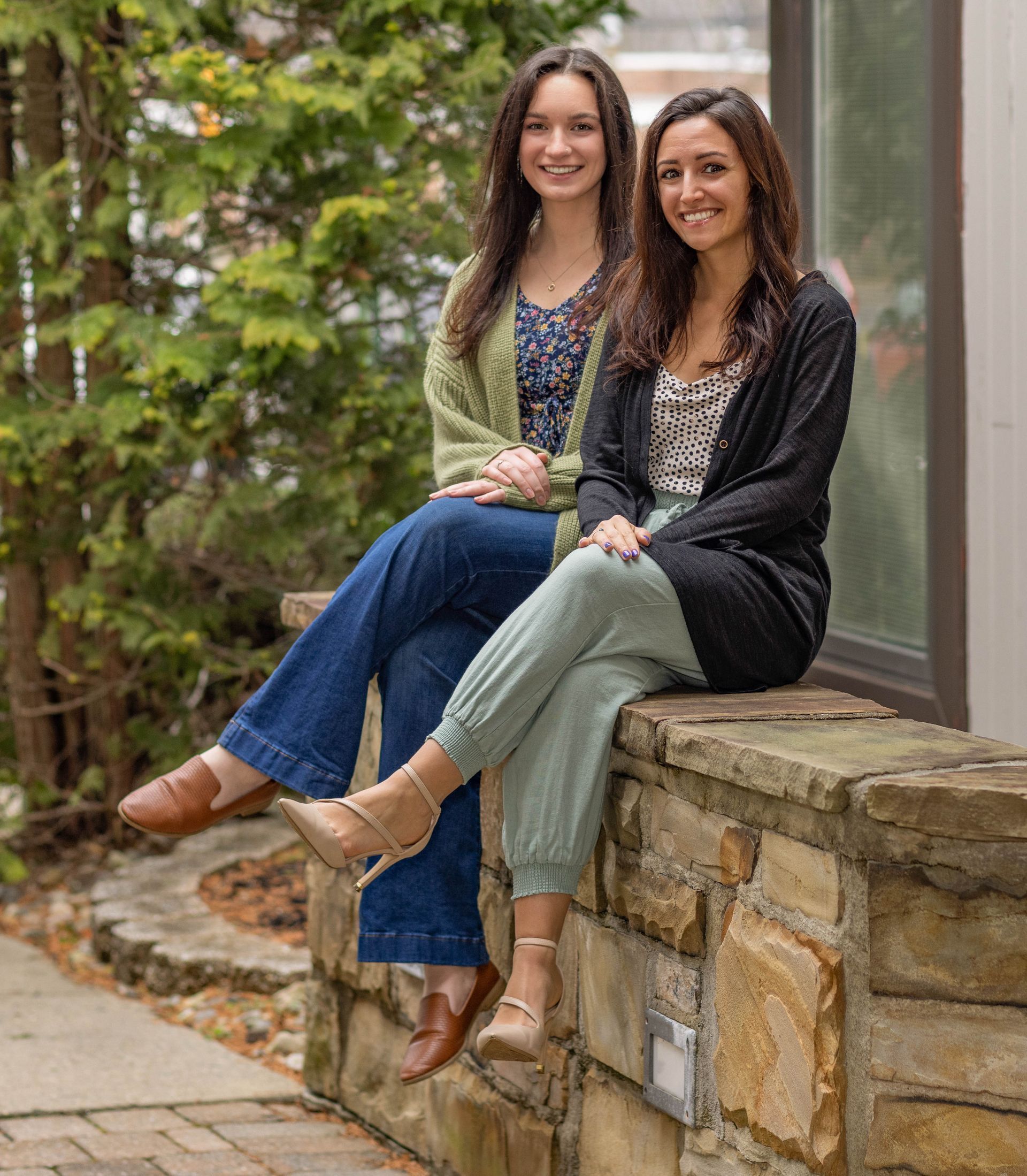 Two women are sitting on a stone wall next to each other.