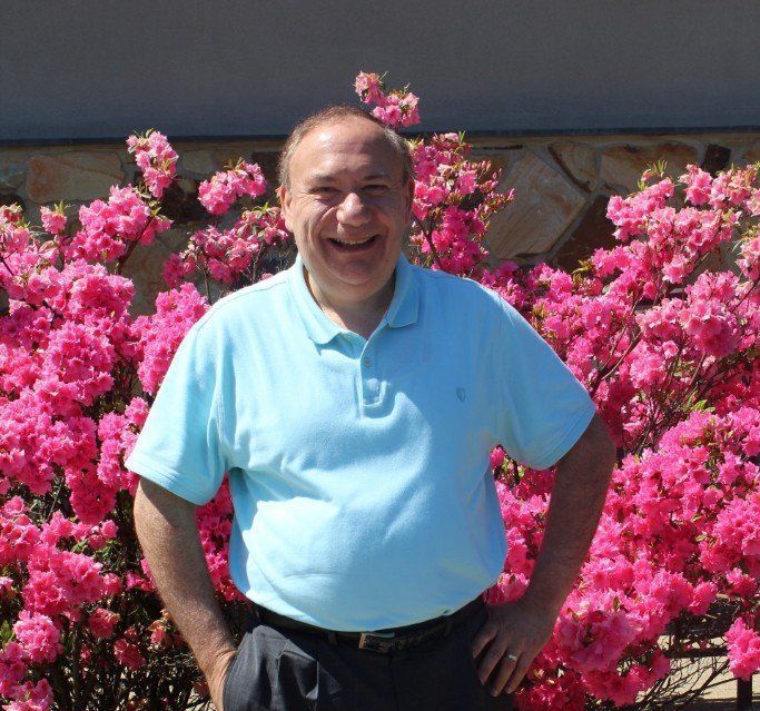 A man in a blue shirt is standing in front of pink flowers