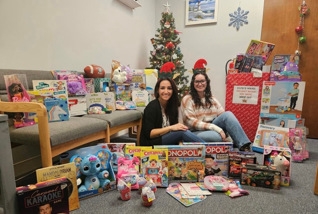 Two women are sitting in front of a christmas tree surrounded by toys.
