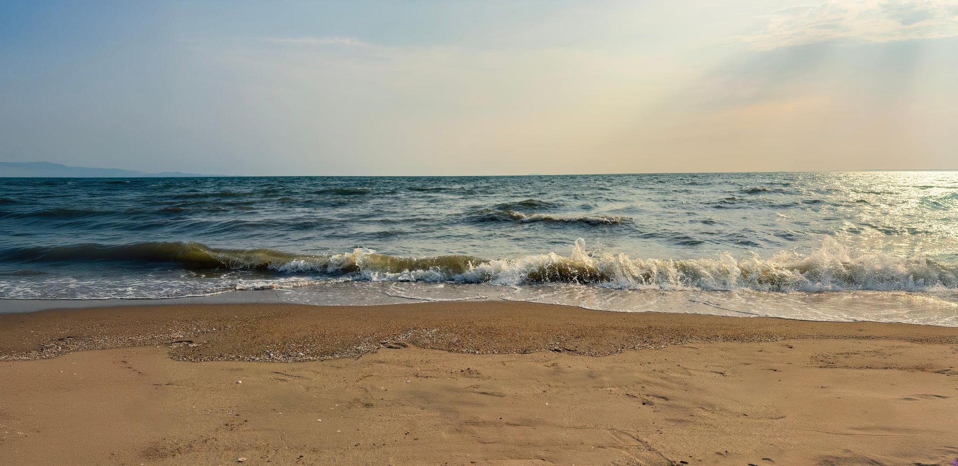 Beach scene with sand, waves, and a clear sky.