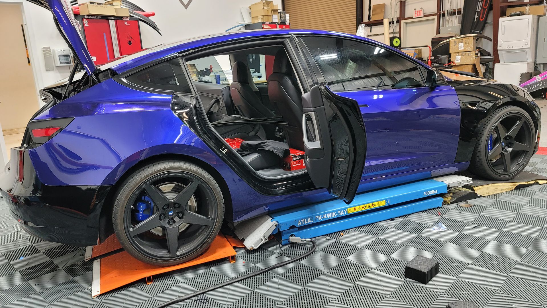 A black tesla model s is sitting on a lift in a garage.