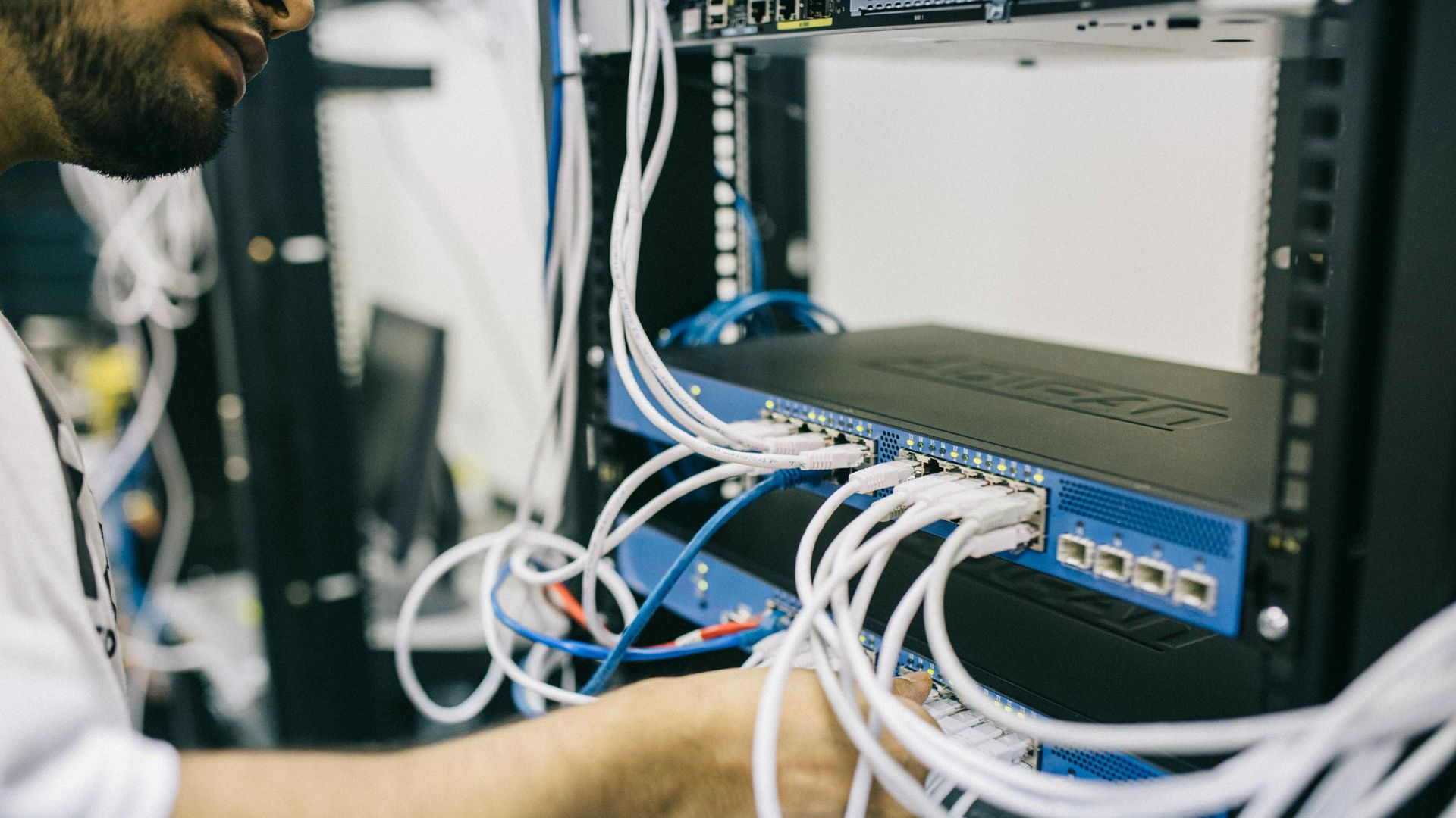 A technician works on network cables connected to a server rack in an office setting.