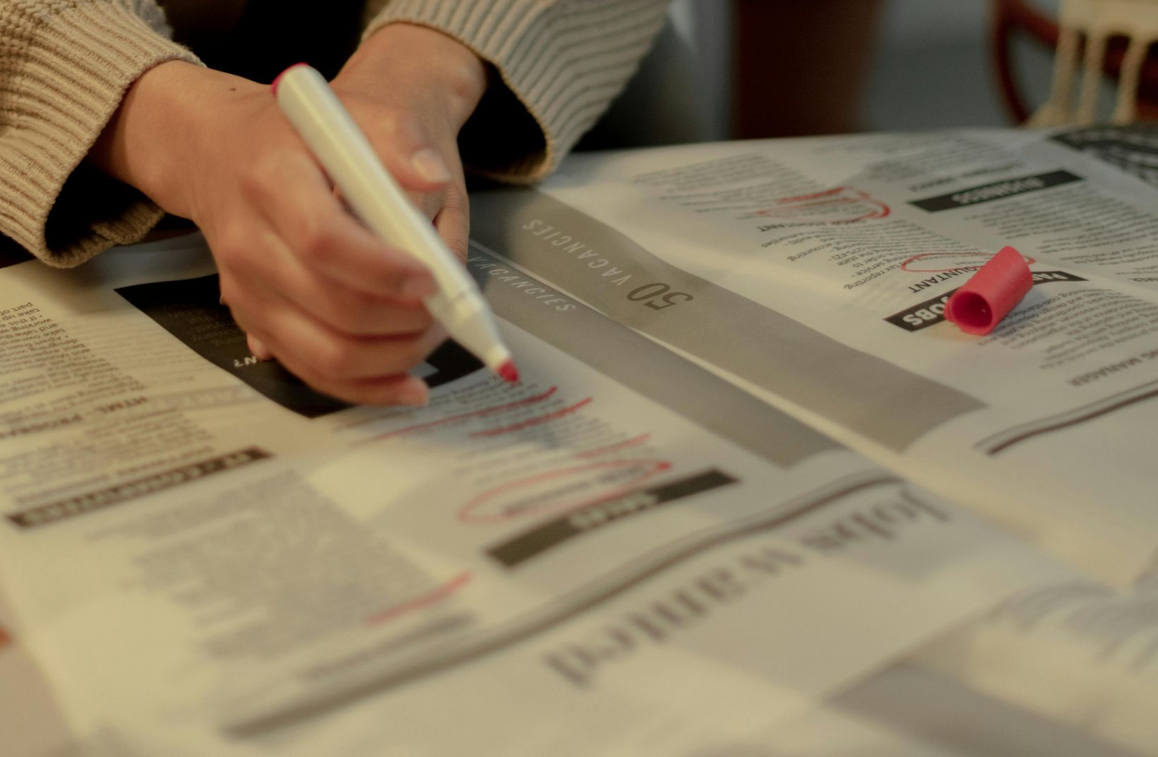 Hands circling job listings in a newspaper with a red marker.