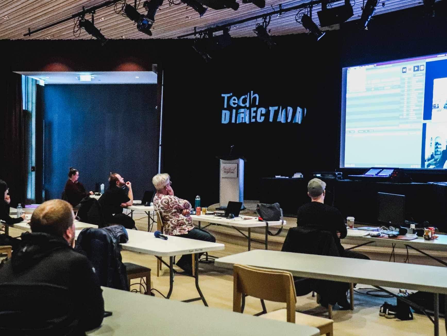 A picture of technicians with computers at tables facing a projected QLab session.