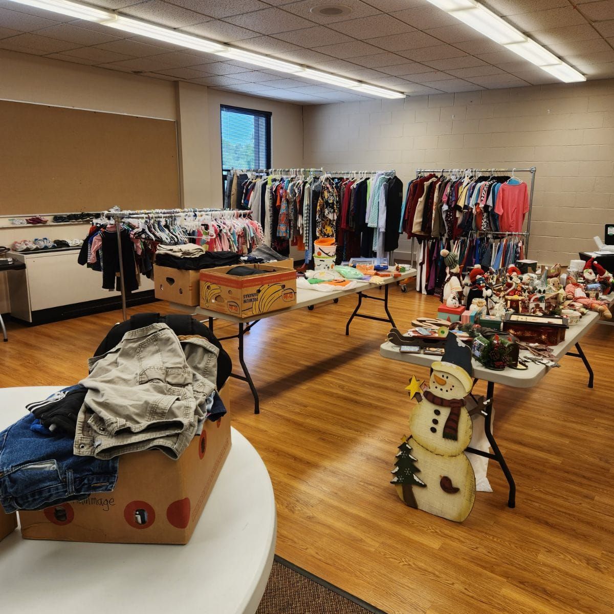 A room with clothes racks and tables displaying items, likely for sale. A snowman decoration is in the foreground.
