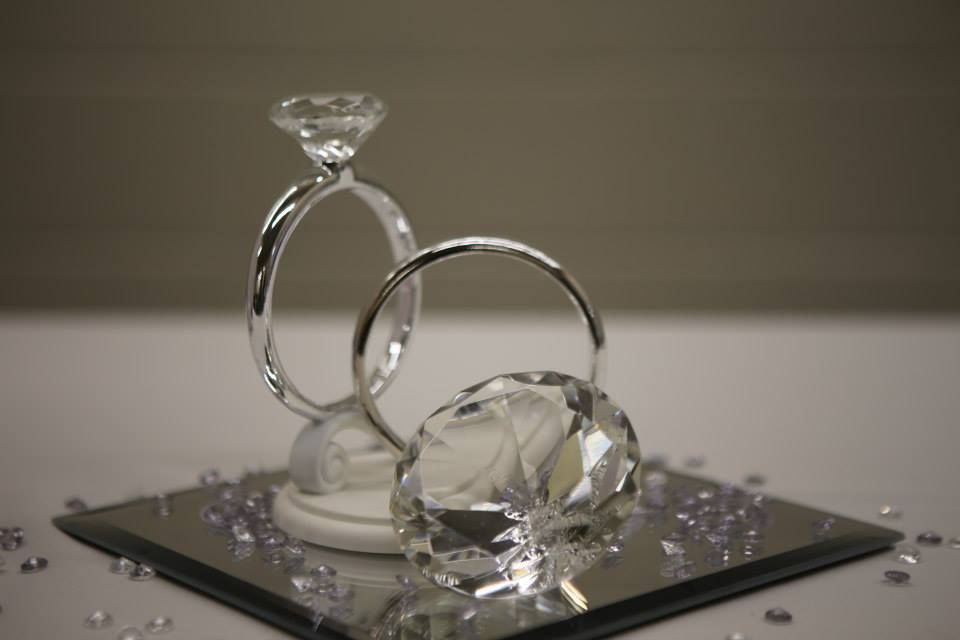 Two decorative diamond rings on a mirrored surface, with scattered purple confetti.