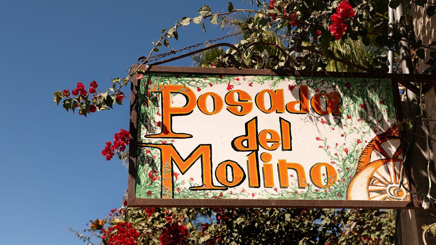 Sign reading “Posada del Molino” with red flowers and blue sky background
