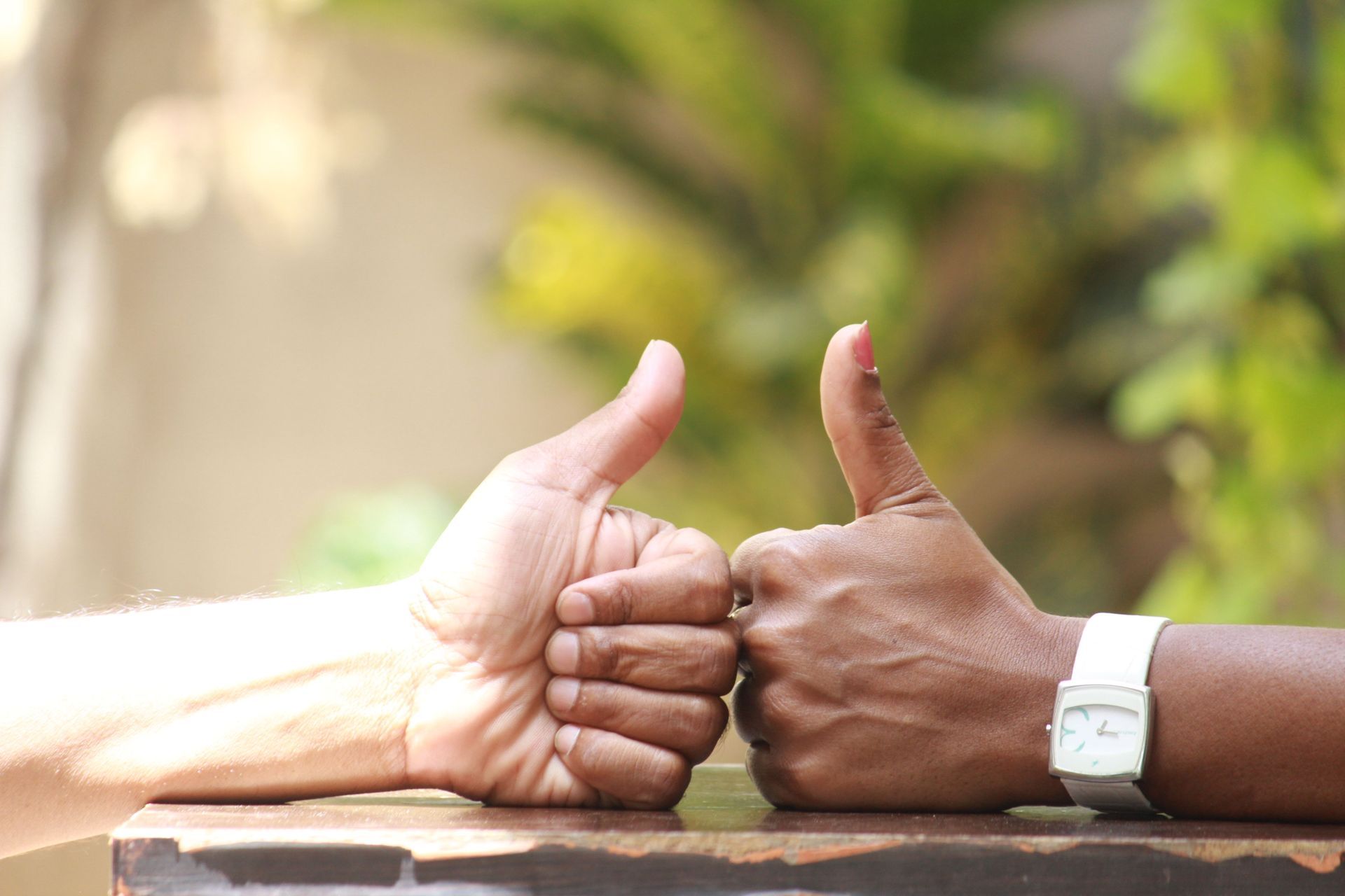 Two people giving thumbs up across a table, one wearing a white watch.