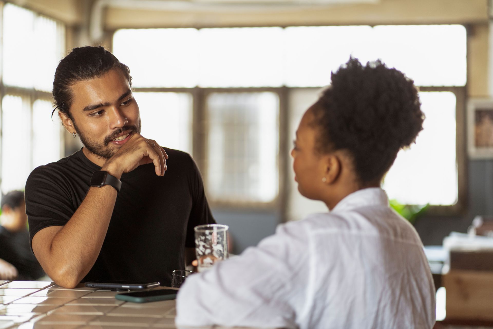 Two people talking about law firm operations across a table in a bright room, one holding a glass