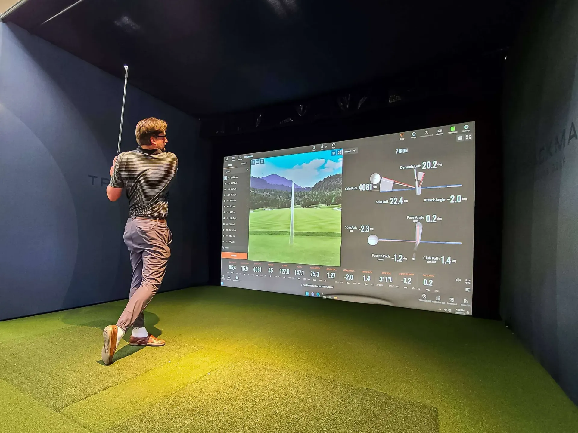 Golfer hitting shot indoors with TrackMan golf simulator display
