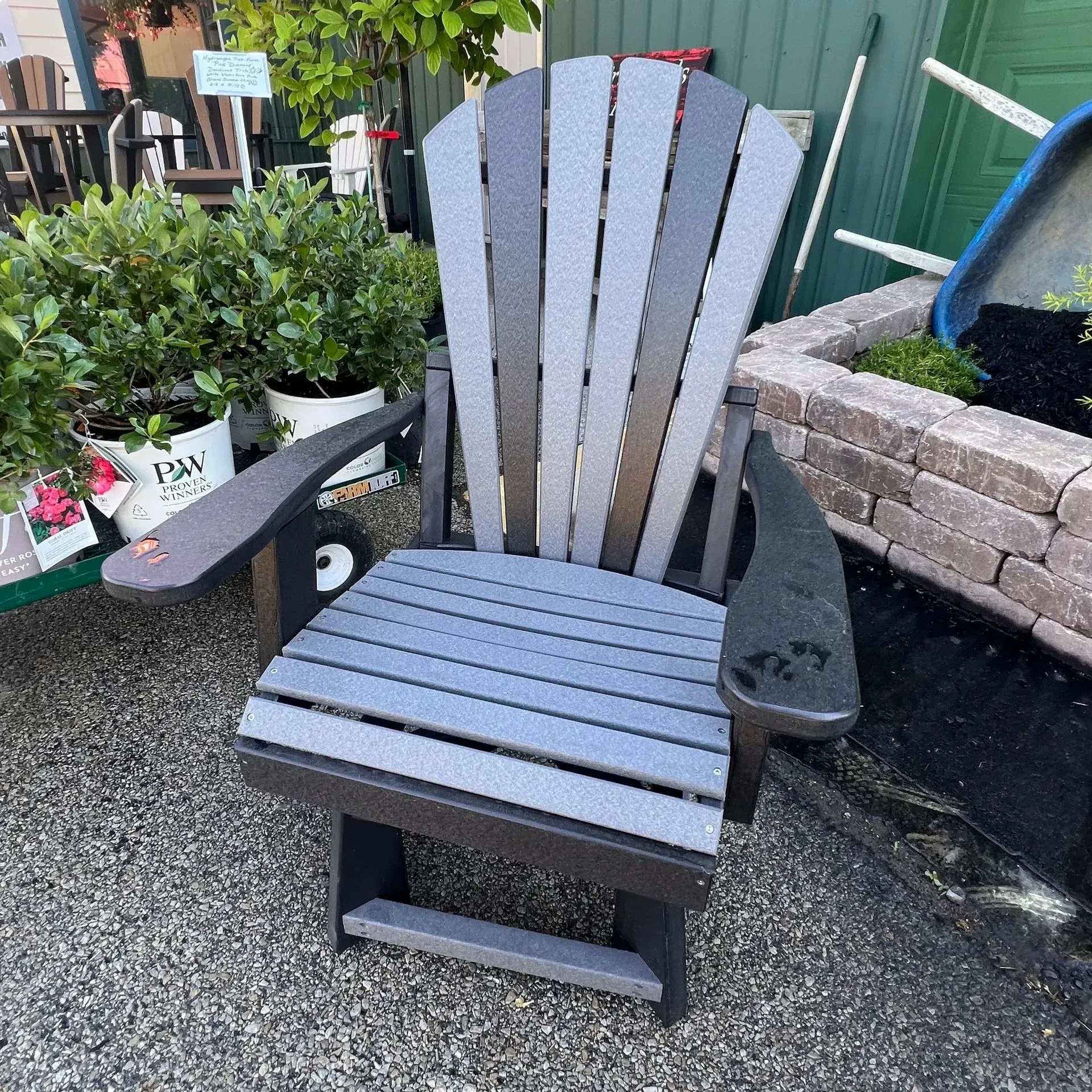 A black and gray adirondack chair is sitting on a gravel road.