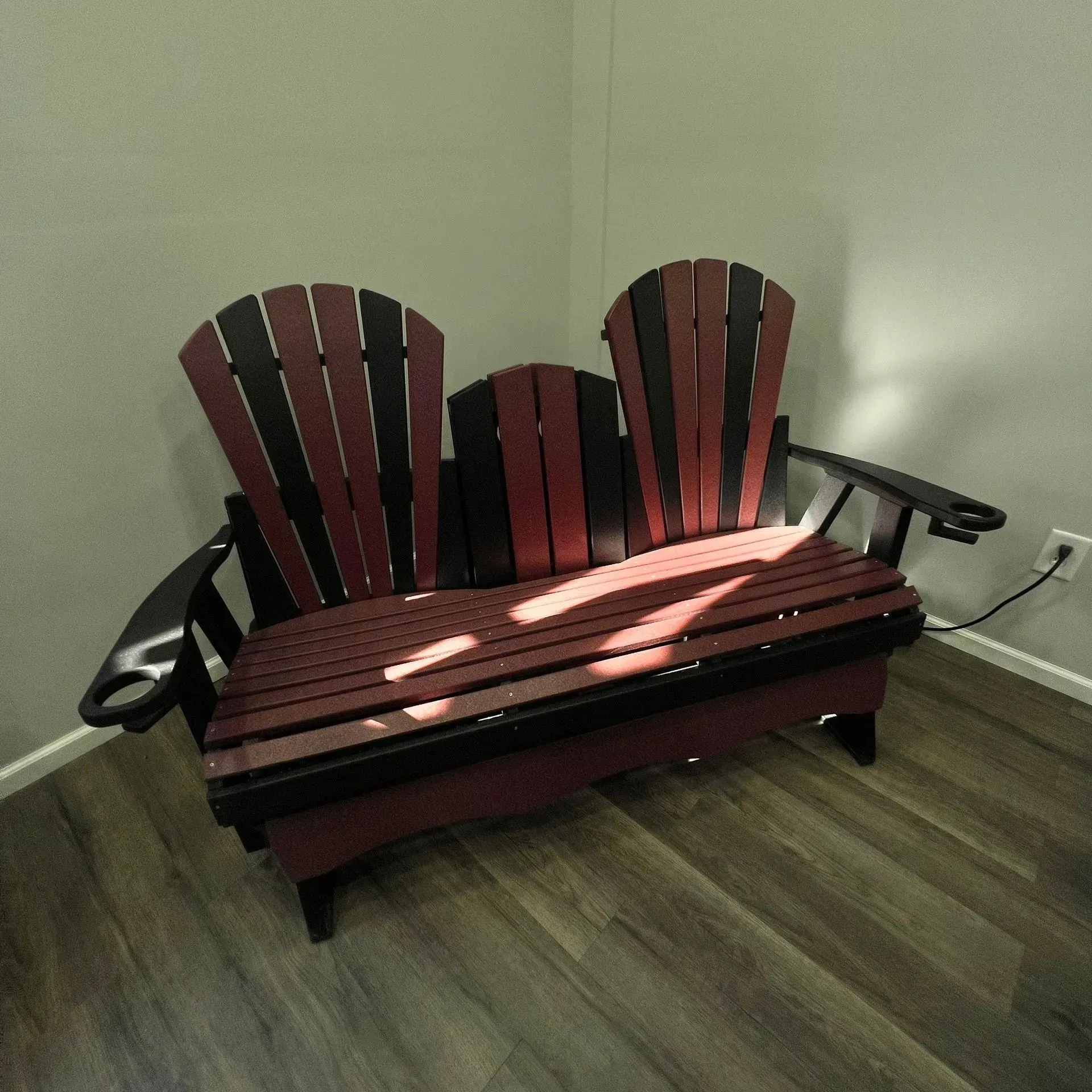 A red and black wooden bench in a corner of a room