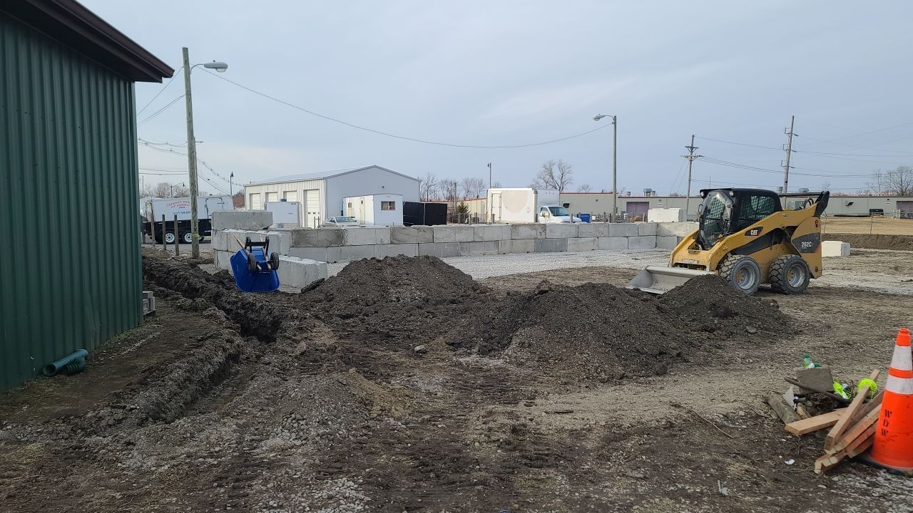 A man is laying in the dirt next to a bulldozer.