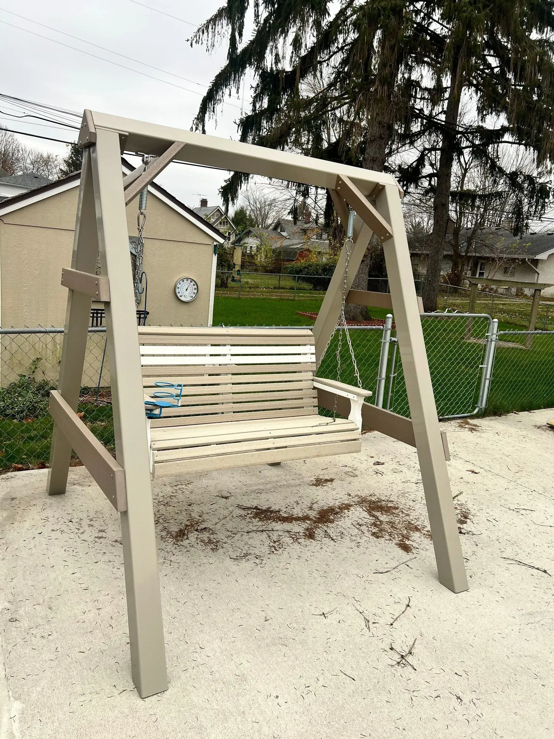 A wooden swing is sitting in the sand in front of a house.