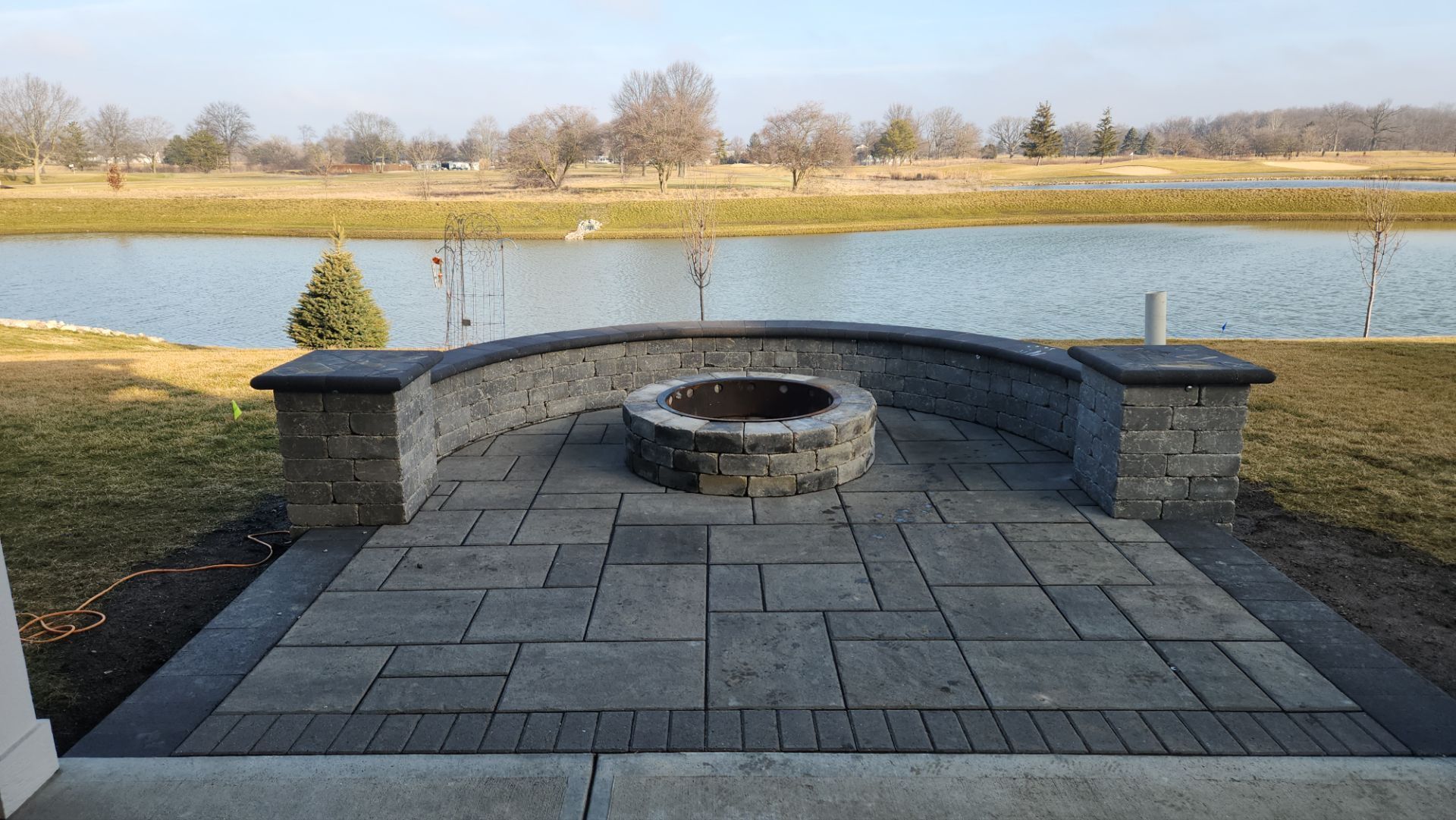 A fire pit is sitting on top of a patio next to a lake.