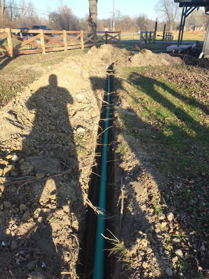 A man is standing in the dirt next to a pipe in the ground.