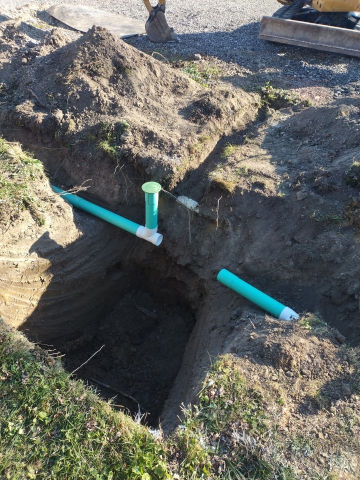 A green pipe is being installed in a hole in the ground.