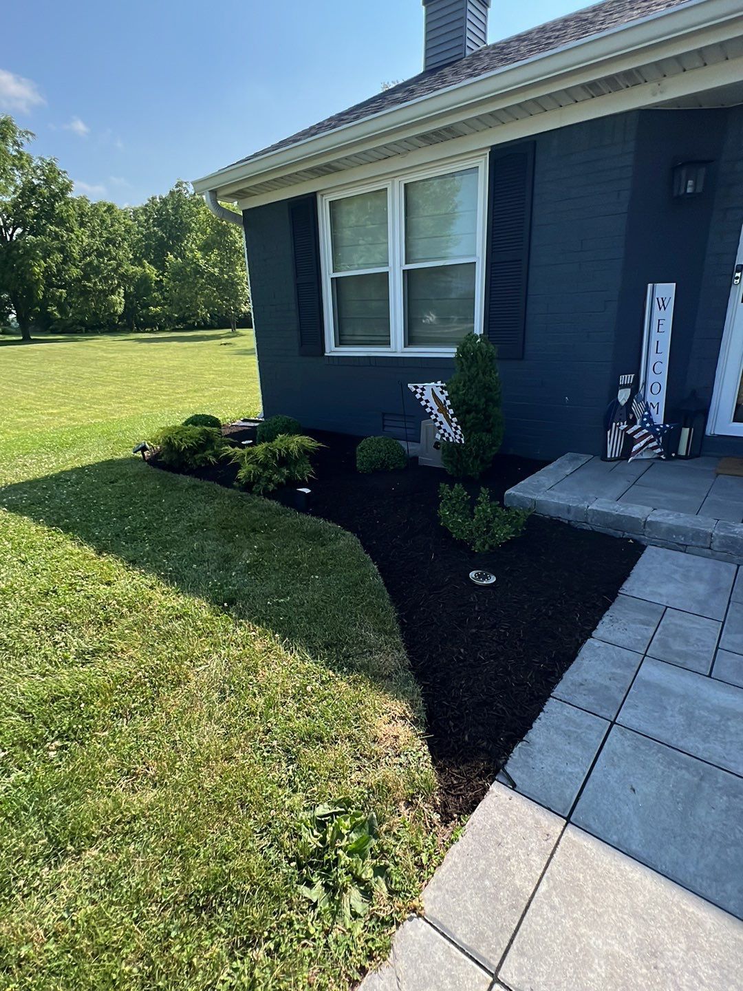 A blue house with black shutters and a lawn in front of it.