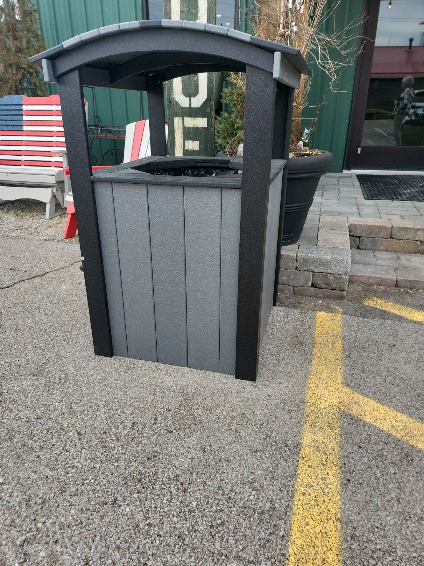 A trash can is sitting in a parking lot next to a yellow line.