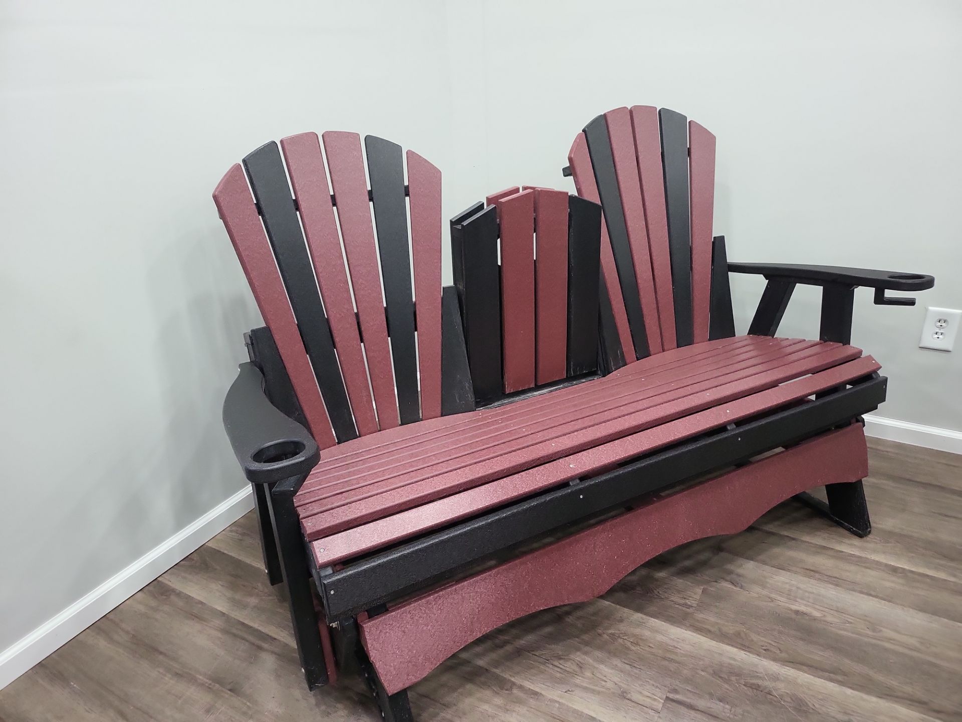 A red and black adirondack chair is sitting on a wooden floor in a room.